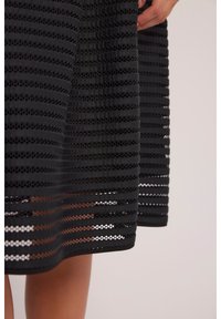 Czarna sukienka w poziome paski, z warstwowanymi wycięciami. Miękka tekstura z równym dołem, odsłaniająca skórę pod otwartymi sekcjami.