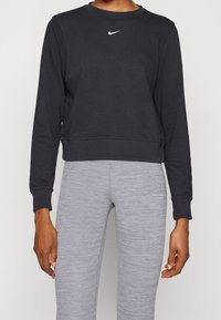 Sweatshirt noir court en tissu lisse, avec un logo Nike blanc sur la poitrine et des poignets côtelés, assorti à un legging gris clair.
