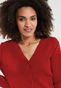 Rode V-hals cardigan gemaakt van zachte brei-materiaal, met een knoopsluiting aan de voorkant en lange mouwen. Glad oppervlak met een getailleerde pasvorm.