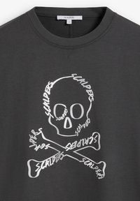 Camiseta de algodón gris oscuro con un gran gráfico de una calavera blanca y huesos cruzados, adornada con la palabra "Scalpers" en una fuente desgastada.