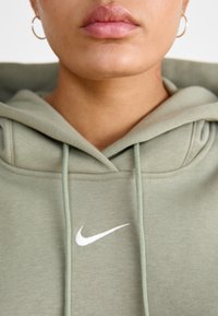 Sweatshirt verde feito de tecido suave, com um bolso frontal, cordões e um logo da Nike branco no peito.