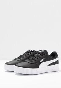 Black leather sneakers with a white stripe design, round toe, textured upper, and white platform sole. Laced closure and logo detail on the tongue.