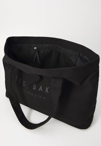 Black canvas tote bag featuring dual handles, an interior zip pocket, and embossed logo lettering on the front. Smooth texture and structured shape.