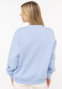 Jasnoniebieska bluza z okrągłym dekoltem, ściągaczami na mankietach i luźnym krojem. Wykonana z miękkiego materiału o gładkiej teksturze, charakteryzująca się minimalistycznym designem.