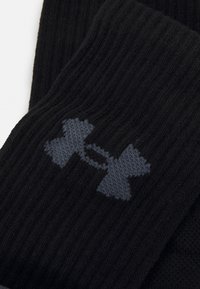 Tejido negro acanalado con un logo gris de Under Armour. El diseño presenta una textura gruesa de punto y un detalle de logo prominente y en contraste.