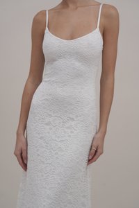 Rochie albă din dantelă cu un corp strâmt, bretele subțiri și o fustă lungă, având modele florale și o textură delicată pe întreaga suprafață.