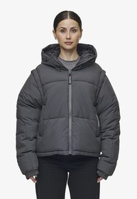 Grå puffjacka med huva, med en dragkedja framtill, ribbade ärmslut och fyrkantig design. Tillverkad av quiltat material med en slät yta.
