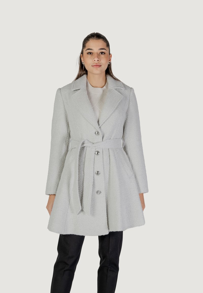 Cappotto grigio testurizzato con vita arricciata, reverse affilati, chiusura con bottoni e due tasche frontali. Abbinato a pantaloni scuri.