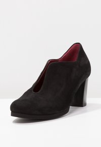 Svart mocka klackskor med mandelformad tå och utskärningsdesign. Inuti har de en kontrasterande röd foder och en robust klack.