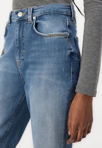 Jeans de mezclilla azul de cintura alta con una textura suave, que cuentan con un bolsillo delantero, un sutil desgaste y un clásico diseño de cinco bolsillos.