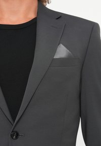 Gray suit jacket with notched lapels, textured fabric, single button closure, and a gray pocket square in the chest pocket. Black undershirt visible.