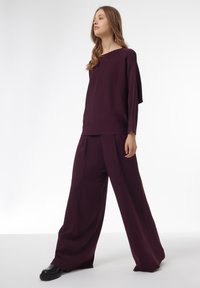Haut tricot bourgogne avec un col bateau, associé à un pantalon large bourgogne à coupe ample. Texture lisse, accents minimaux, silhouette moderne.