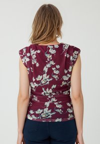 Top floreale bordeaux con maniche corte, caratterizzato da motivi di fiori bianchi e gialli, tessuto morbido e design arricciato in vita.