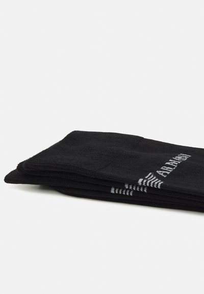 Schwarze Baumwollsocken gestapelt, mit einem strukturierten Design und weißer Branding auf der Seite. Der Stoff wirkt weich und dehnbar.