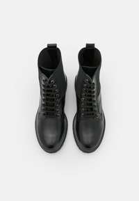 Botines negros con una puntera de cuero suave, caña de tela, ojales metálicos y una suela de goma con un patrón de tacos.
