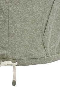 Tissu vert clair chiné avec des coutures visibles et un cordon blanc noué au bord inférieur du vêtement.