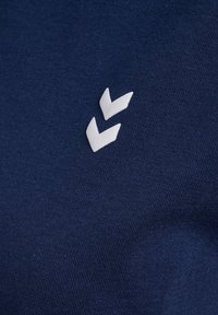 Mörkblått tyg med en slät struktur och en vit zigzaglogotyp i nedre hörnet. Enkel design utan ytterligare mönster.