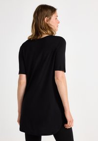 Svart tunika topp med korta ärmar, med rundad nederkant och jämn textur. Baksidan visar en avslappnad passform och minimala designdetaljer.