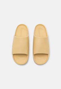 Paire de sandales beige à enfiler avec semelles côtelées et larges brides, vues de dessus sur un fond blanc uni.