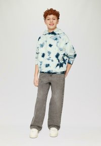Lichtblauwe tie-dye hoodie met marineblauwe patronen, gecombineerd met grijze wijde jeans en witte sneakers. Zacht materiaal, relaxte pasvorm, vooraan een kangoeroezak.