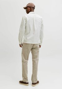 Chemise blanche boutonnée, pantalon en velours côtelé beige, baskets marron. Le modèle porte une casquette marron et est vu de dos, légèrement tourné vers la gauche.