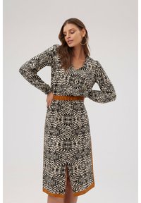 Sukienka z długim rękawem w czarno-kremowy abstrakcyjny wzór, z zaakcentowaną talią i pomarańczowym paskiem, z dekoltem z przodu.