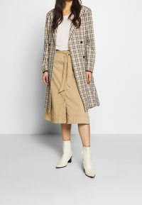 Checked coat with yellow, black, and white pattern, beige skirt, and white ankle boots. Coat features double-breasted design and buttons.