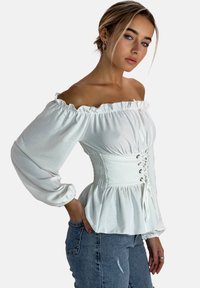 Weißes schulterfreies Blusenshirt mit rüschigem Ausschnitt, gerafftem Taillenbereich und Schnürdetails vorne. Sanfter Stoff mit Ballonärmeln.
