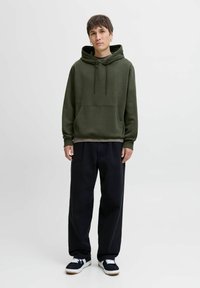 Olive green hoodie with long sleeves, front pocket, and drawstrings, paired with black wide-leg pants and black sneakers with white accents.