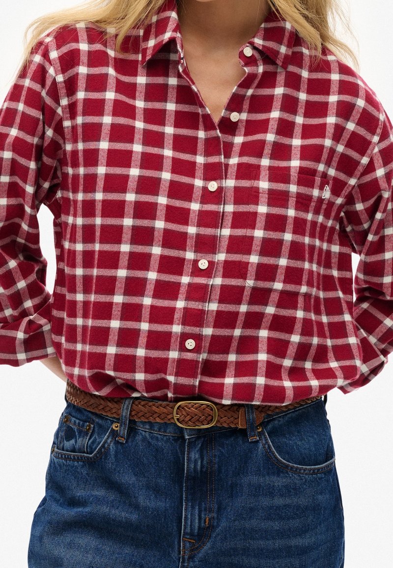 Camicia a quadri rossa e bianca in flanella con collo abbottonato, caratterizzata da una tasca sul petto e una cintura intrecciata marrone con fibbia dorata.