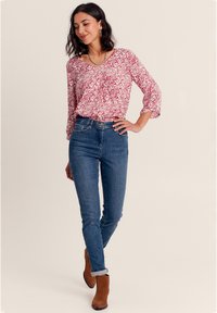 Rot-weiße gemusterte Bluse mit Dreiviertelärmeln, kombiniert mit dunkelblauen Skinny-Jeans und braunen Stiefeletten.