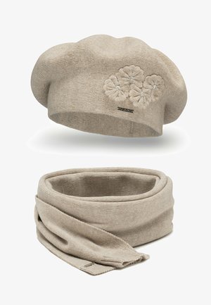 Beige strikket beret med blomsterbroderi og udsmykninger, parret med et matchende beige tørklæde, begge med en blød tekstur.