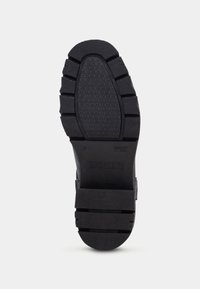 Suela de zapato de goma negra con surcos texturizados, que presenta un patrón geométrico ligeramente elevado. Los detalles de marca y talla son visibles.
