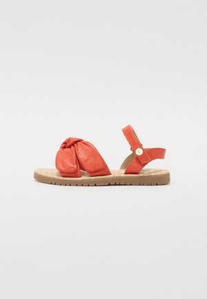 Orangefarbene Leder-Sandale mit einem Knoten-Detail an der Zehe, verstellbarem Knöchelriemen und einer tanfarbenen Gummisohle mit Profil.