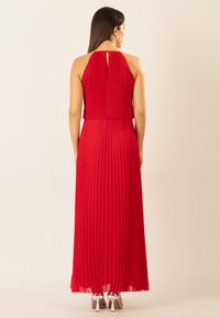 Langes rotes Faltenkleid mit Halterneck, Rückenausschnitt und fließendem Rock, kombiniert mit silbernen High-Heels.