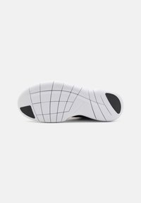 Sulan på en sko med texturerat vitt gummimaterial, med svarta accenter, ett rutmönster och en distinkt Nike-logga på sidan.