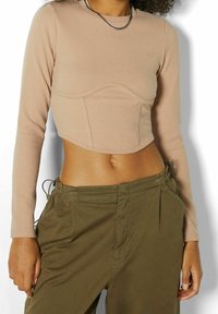 Femme portant un haut court côtelé beige à manches longues et un pantalon ample vert olive avec des cordons de serrage latéraux.