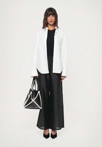 White button-up shirt over a black top, paired with black wide-leg pants. Black handbag with white decorative stitching, black pointed heels.