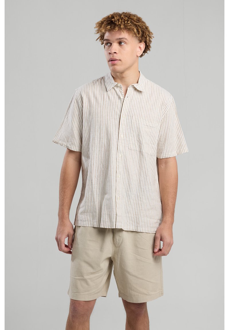 Camicia a maniche corte a righe in beige e crema, con chiusura a bottoni sul davanti, taschino singolo sul petto, abbinata a pantaloni corti beige. Tessuto liscio e leggero.