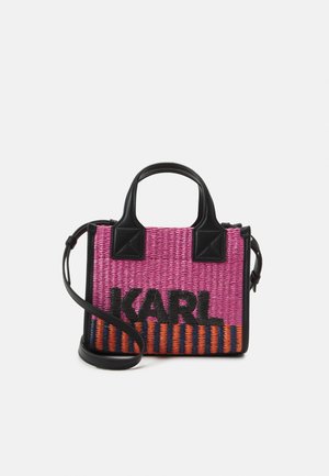 Pieni suorakulmainen kudottu käsilaukku vaaleanpunaisilla ja oransseilla raidoilla, mustilla kahvoilla ja mustalla säädettävällä olkahihnalla, jossa lukee "KARL" mustilla kirjaimilla.