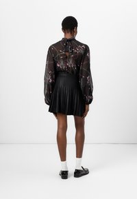 Blusa nera trasparente con motivi floreali, con nodo al collo e schiena scoperta; abbinata a una gonna a pieghe nera aderente e scarpe nere.