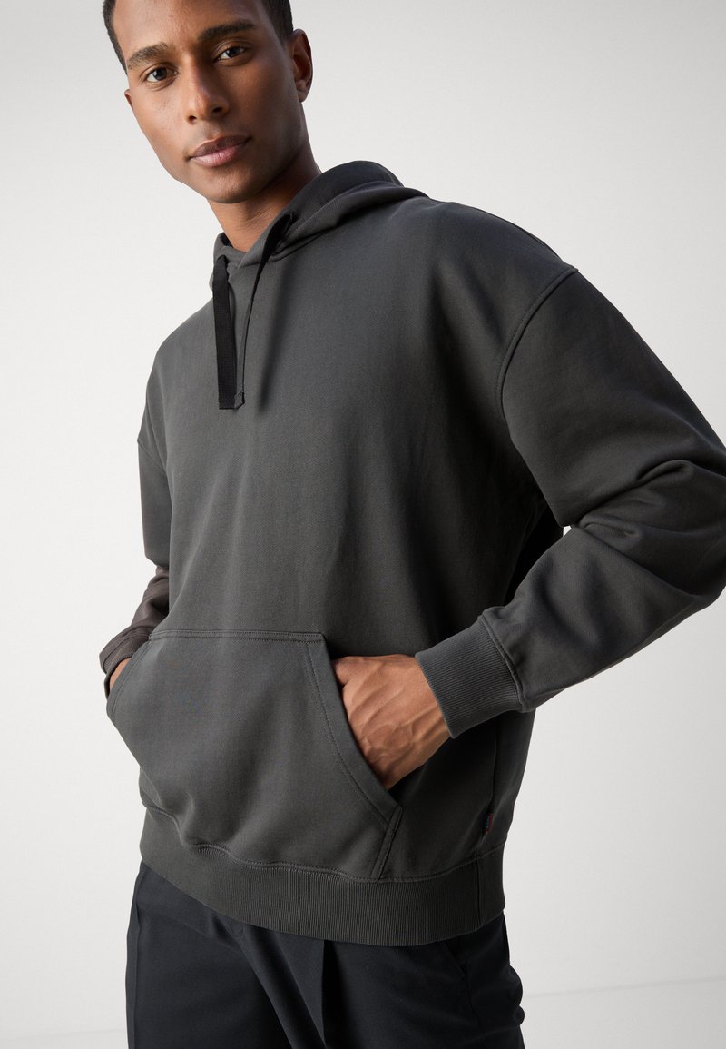 Donkergrijze hoodie met een buidelzak, verstelbare trekkoordcapuchon en ribgebreide manchetten en zoom. De stof lijkt zacht en gestructureerd.