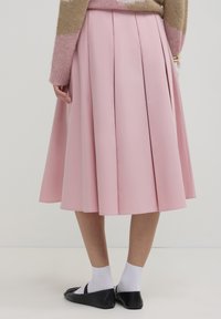 Gonna pieghettata rosa realizzata in tessuto morbido, che arriva a metà polpaccio. Abbinata a ballerine nere e calzini bianchi alla caviglia, creando un look a strati.