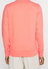 Rozpinany sweter w kolorze koralowym z długimi rękawami, okrągłym dekoltem oraz ściągaczami na rękawach i u dołu. Miękka faktura, prosty design, bez widocznych logo czy wzorów.