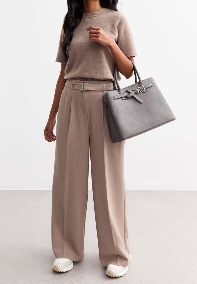 Beige stickad tröja, vida beige byxor och en grå läderhandväska. Anmärkningsvärda detaljer: texturerad tyg, strukturerad handväska design, vita sneakers.