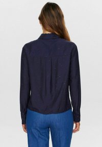 Marineblå skjorte med lange ærmer, der har en rygstykke og flerfarvede prikker. Lavet af glat, let stof.