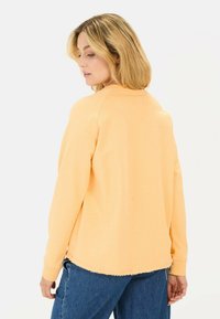 Langærmet sweatshirt med rund hals i lys orange stof med en afslappet pasform, der har frynsede kanter og ribbede manchetter. Kombineret med denim.