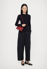 Marine blauwe lange mouw top met knoopsluiting, wijdvallende zwarte broek en een kleine rode crossbody tas. Zwarte instap schoenen met accenten.