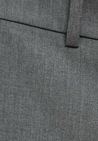 Sivi materijal s glatkom teksturom i suptilnim dijagonalnim tkanjem, sa malim, usklađenim petljom za pojas na vrhu.