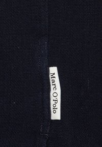 Tessuto blu navy con superficie texturizzata; presenta un piccolo etichetta bianca con la scritta "Marc O'Polo". Nessun motivo o dettaglio visibile.